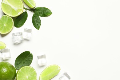 Fresh ripe limes with green leaves and ice cubes on white background, flat lay