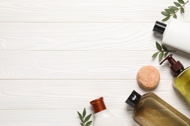 Photo of Shampoo bottles, leaves and solid shampoo bar on white wooden table, flat lay. Space for text