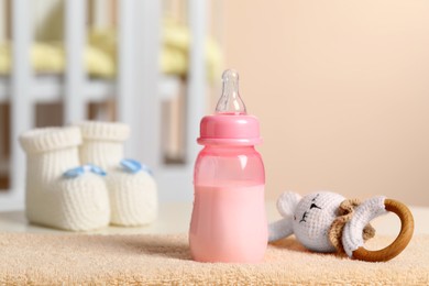 Photo of Feeding bottle with milk, toy and booties on table indoors