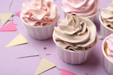 Photo of Delicious birthday cupcakes, sprinkles and bunting flags on violet background, closeup