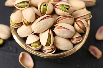 Photo of Tasty pistachios in bowl on black table, closeup