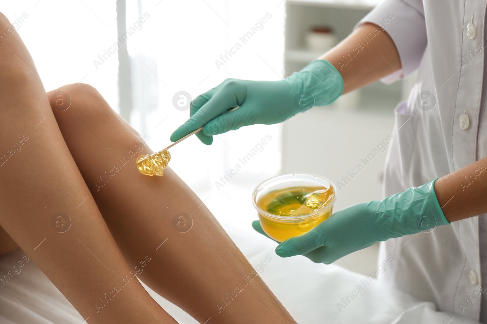 Photo of Woman getting wax epilation of legs in salon, closeup