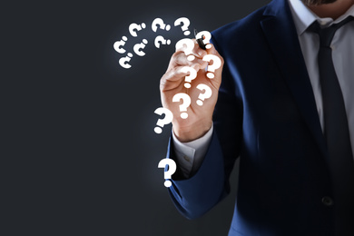 Image of Businessman using virtual screen with question mark symbols on dark background, closeup