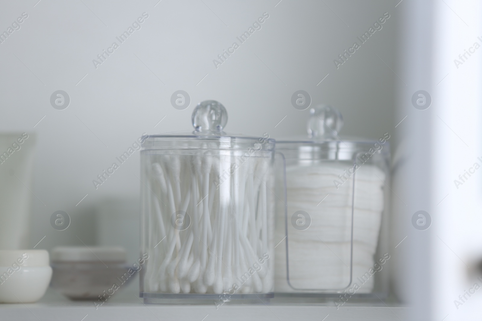 Photo of Cotton buds and pads in transparent holders on shelf, closeup