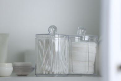 Cotton buds and pads in transparent holders on shelf, closeup