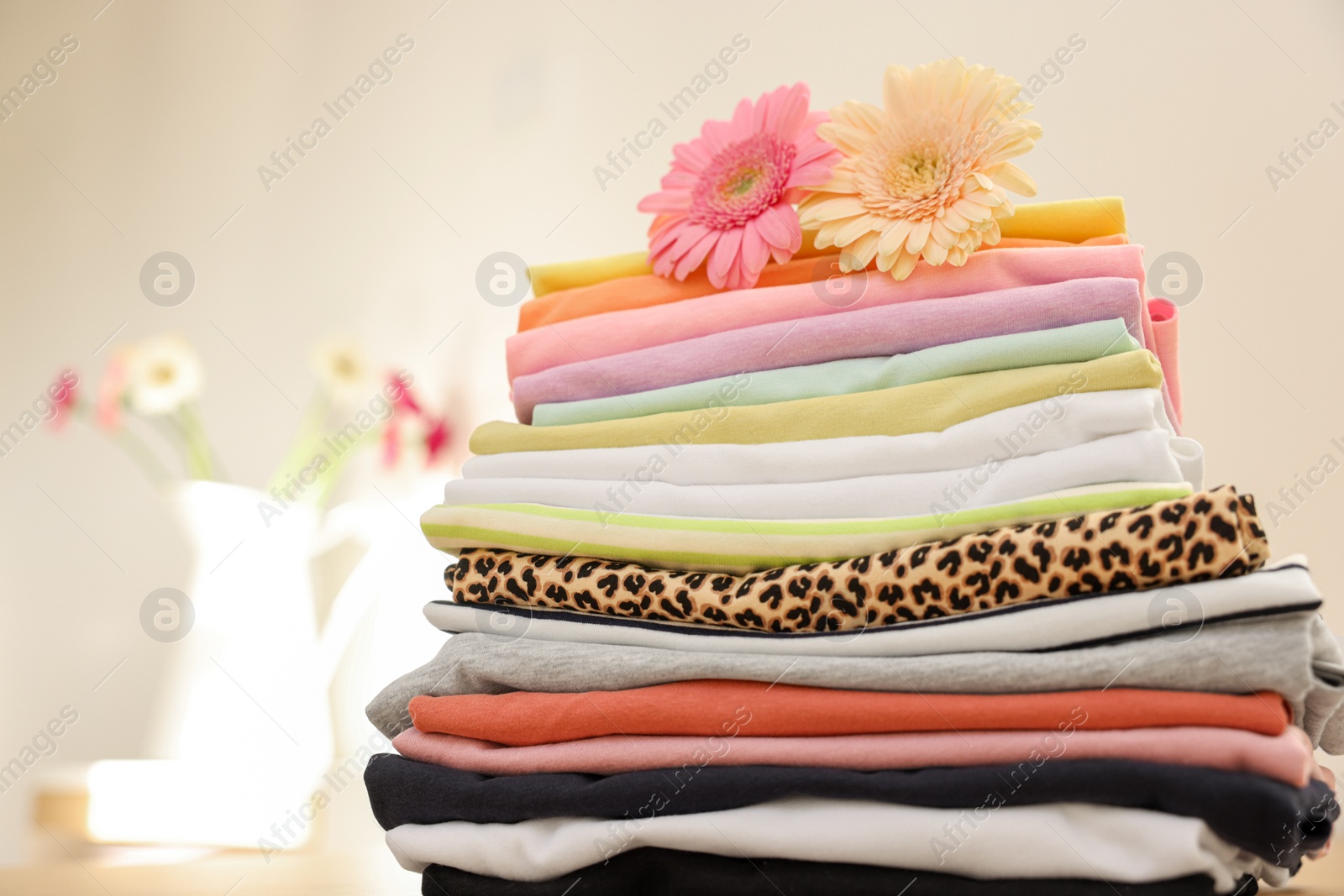 Photo of Stack of clean clothes and flowers on blurred background, closeup