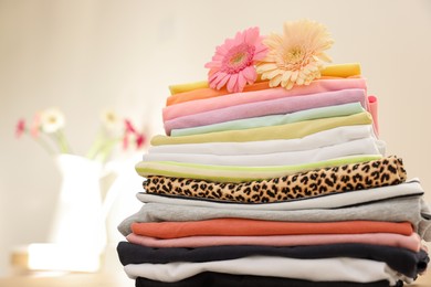 Stack of clean clothes and flowers on blurred background, closeup