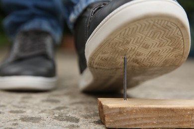 Photo of Careless man stepping on nail in wooden plank outdoors, closeup