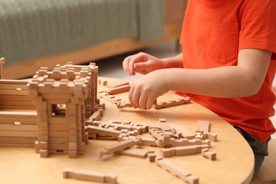 Photo of Little boy playing with wooden construction set at table in room, closeup. Child's toy