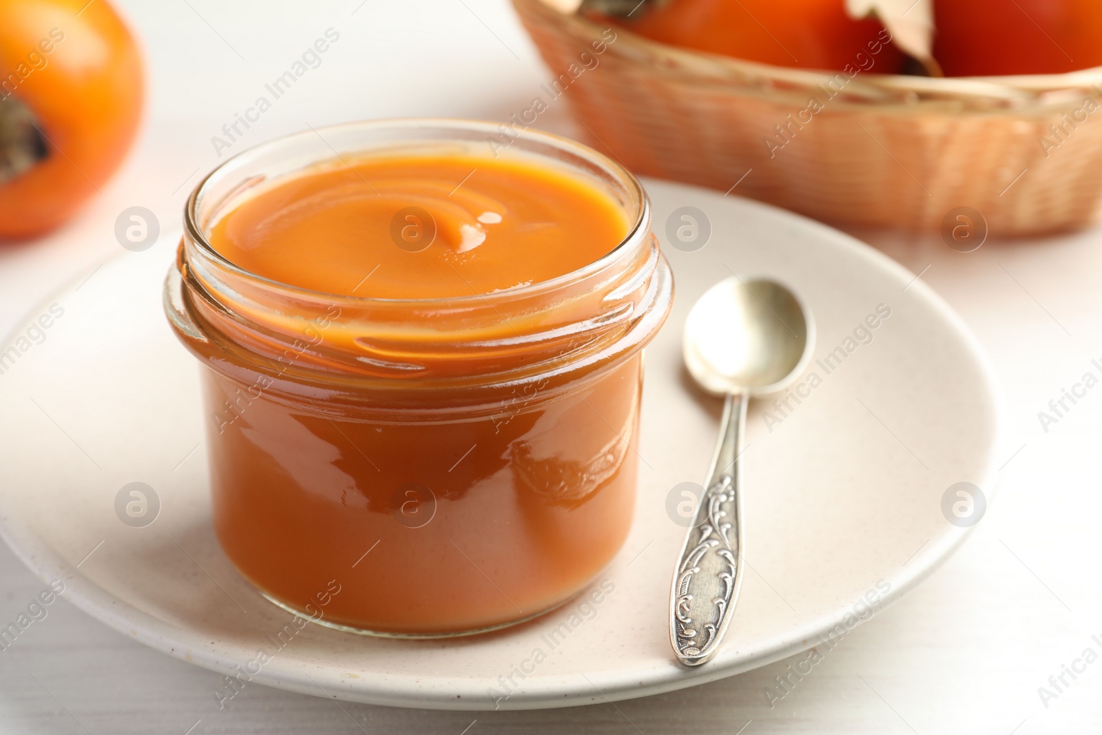 Photo of Delicious persimmon jam in glass jar served on white wooden table, closeup