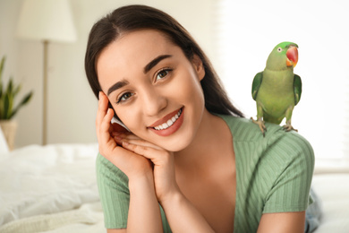 Young woman with Alexandrine parakeet indoors. Cute pet