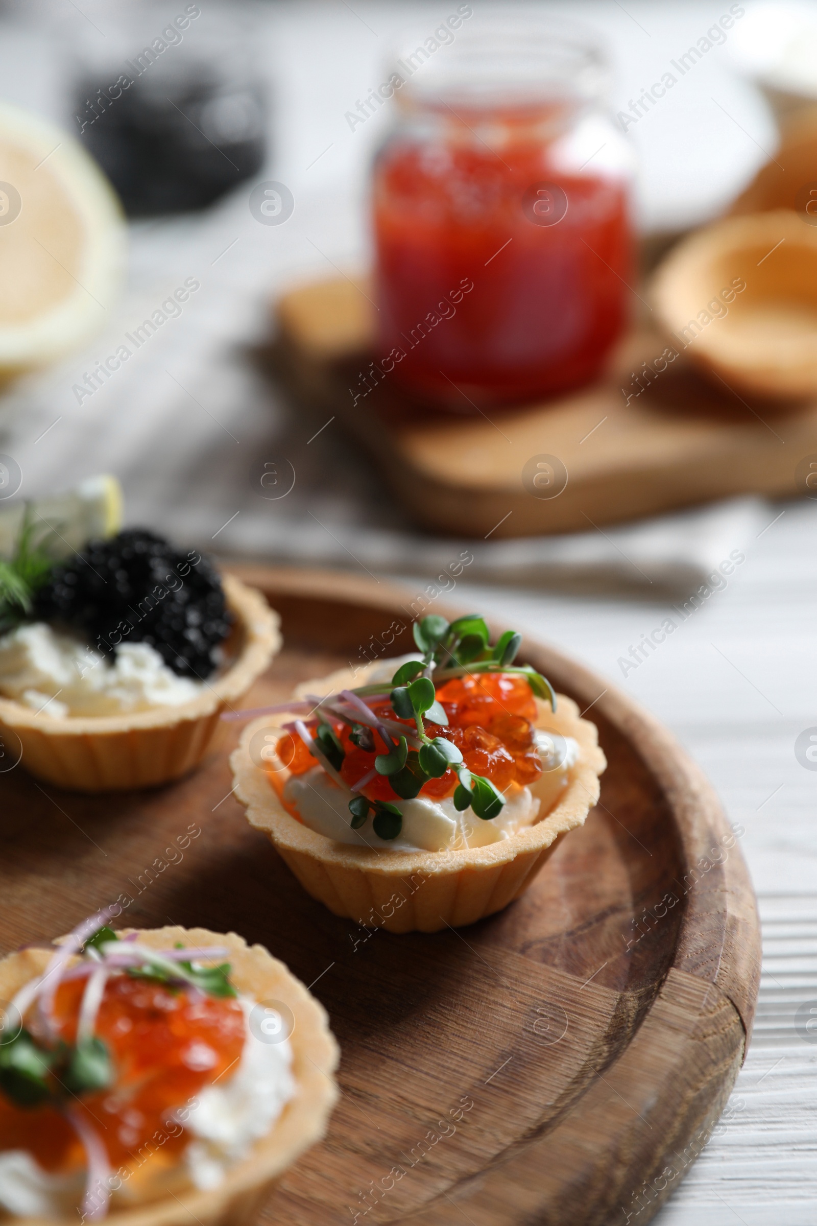 Photo of Delicious tartlets with red and black caviar served on white wooden table, closeup. Space for text