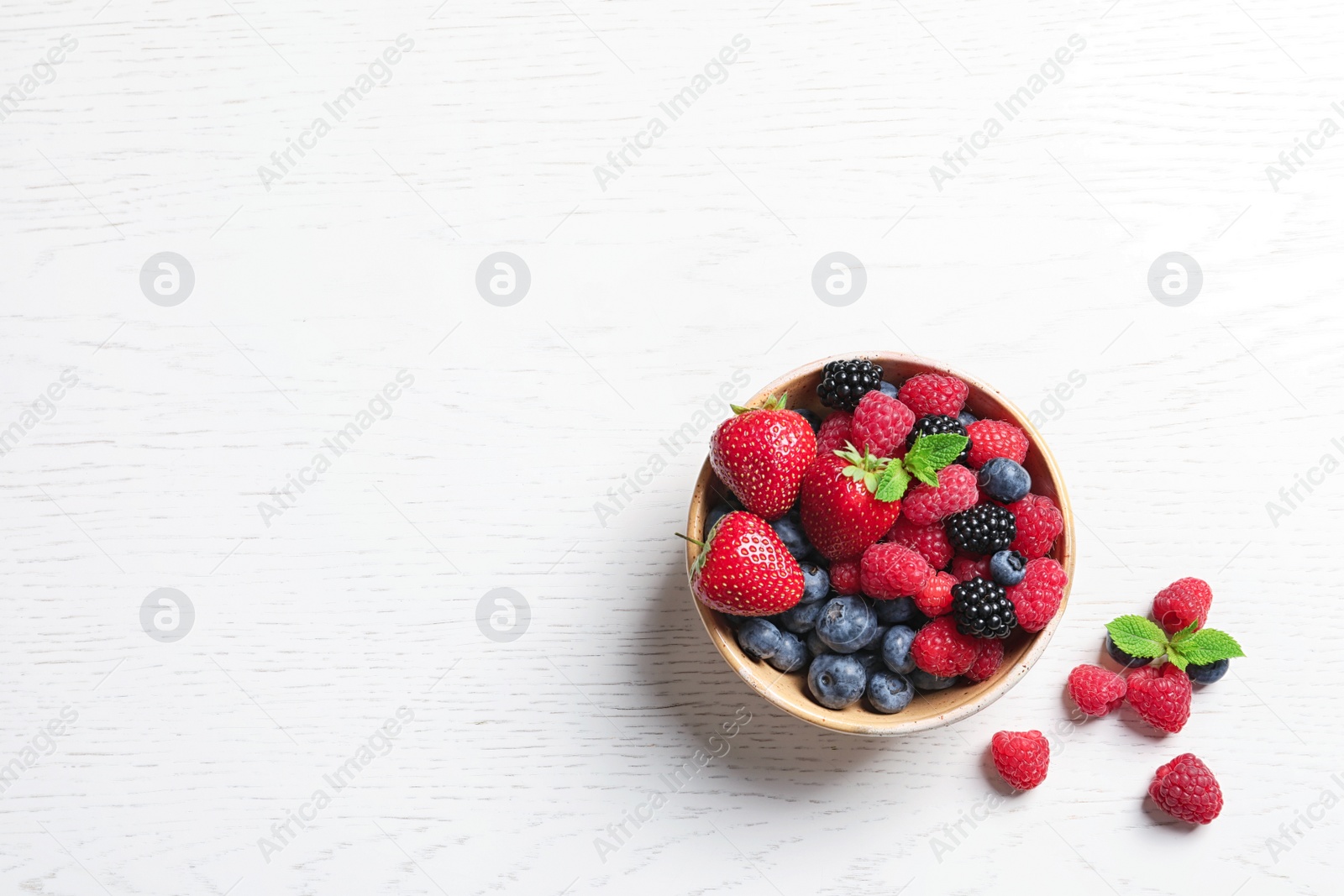 Photo of Bowl with raspberries and different berries on wooden table, top view