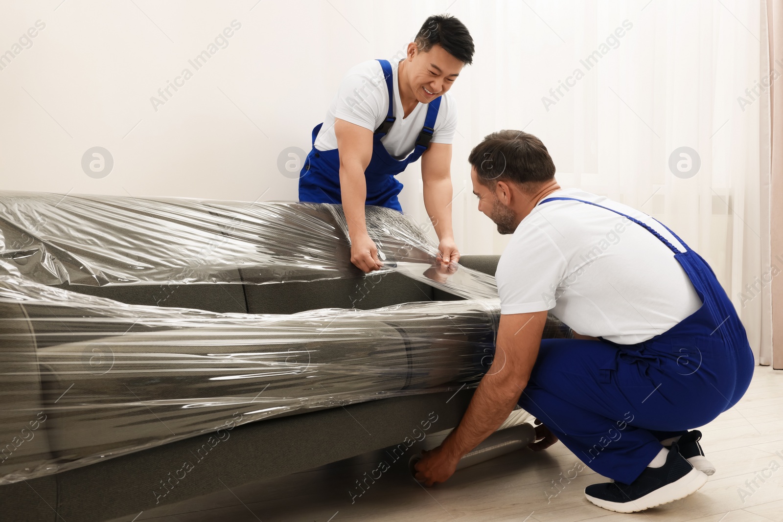 Photo of Workers wrapping sofa in stretch film indoors