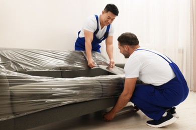Photo of Workers wrapping sofa in stretch film indoors