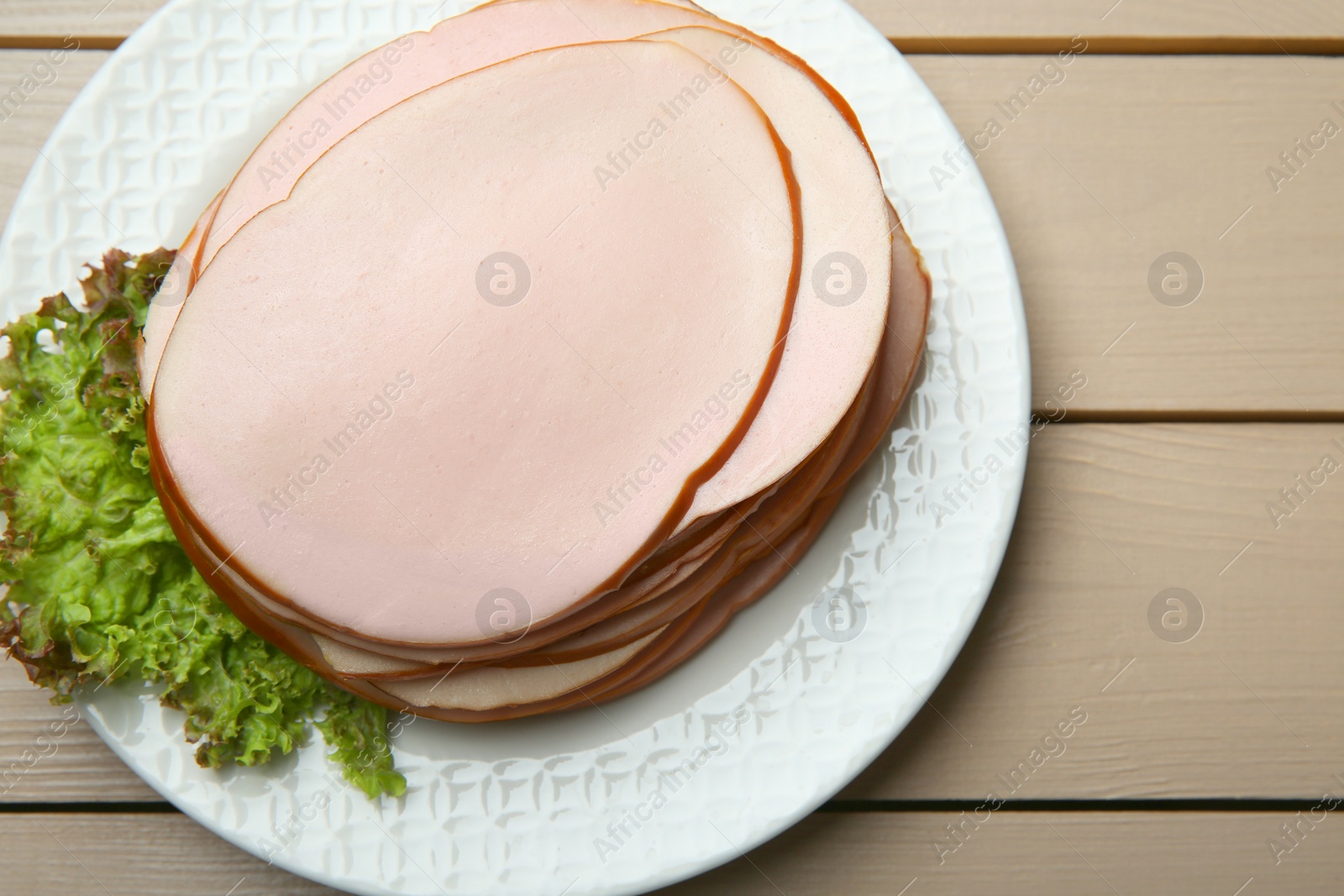 Photo of Slices of delicious boiled sausage with lettuce on beige wooden table, top view