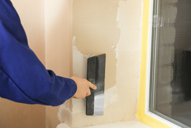 Photo of Professional worker plastering window area with putty knife indoors, closeup. Interior repair