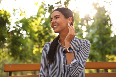 Photo of Young woman with wireless earphones in park