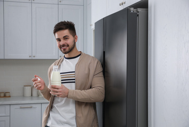 Young man with bottle of milk near refrigerator in kitchen