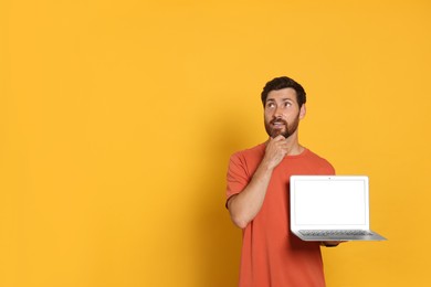 Photo of Thoughtful handsome man with laptop on orange background