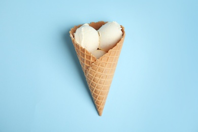 Photo of Delicious vanilla ice cream in wafer cone on blue background, top view