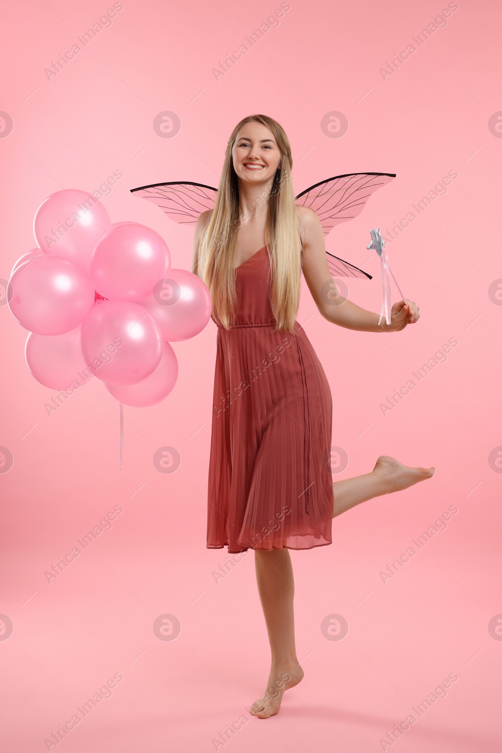 Photo of Beautiful girl in fairy costume with wings, magic wand and balloons on pink background