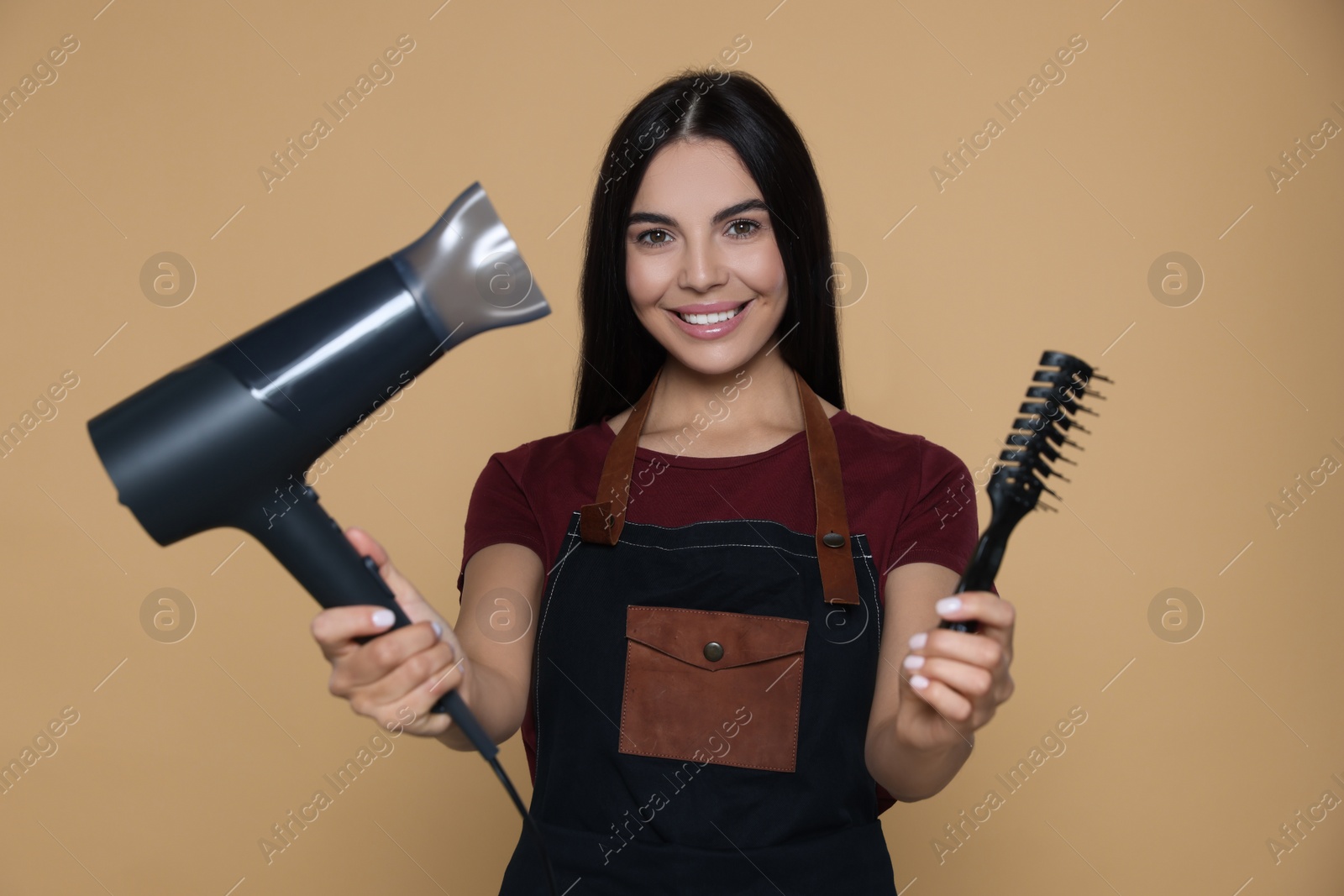 Photo of Portrait of happy hairdresser with hairdryer and vent brush on beige background