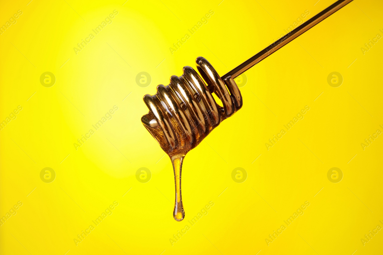 Photo of Dripping honey from dipper on yellow background, closeup