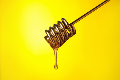 Photo of Dripping honey from dipper on yellow background, closeup