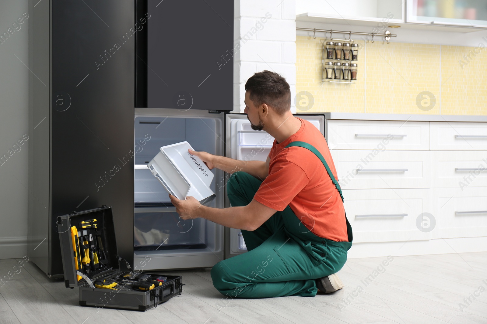 Photo of Professional male technician repairing broken refrigerator indoors