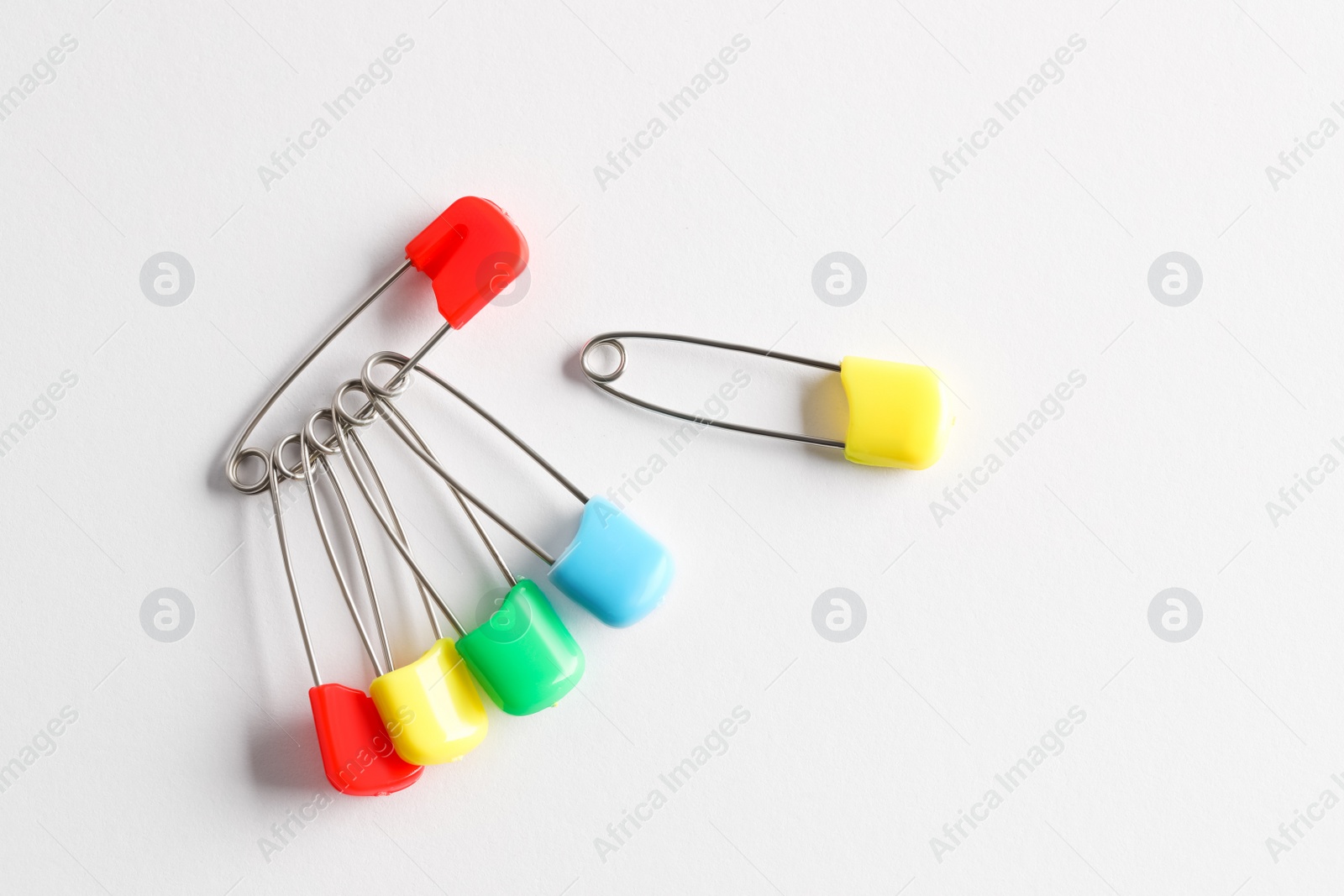 Photo of Colorful safety pins on white background, flat lay. Space for text