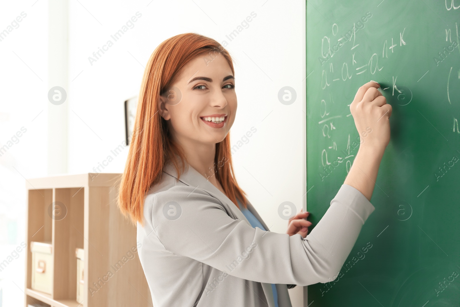 Photo of Beautiful young teacher writing on blackboard in classroom