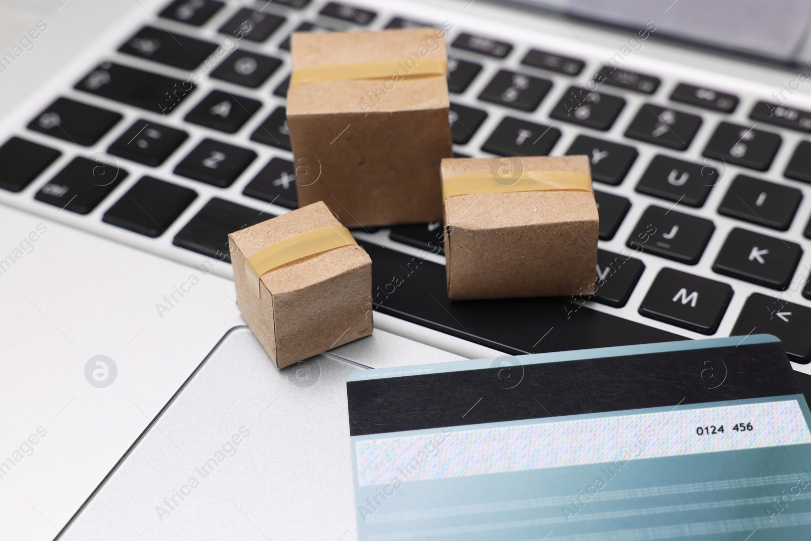 Photo of Internet shopping. Small cardboard boxes and credit card on laptop, closeup