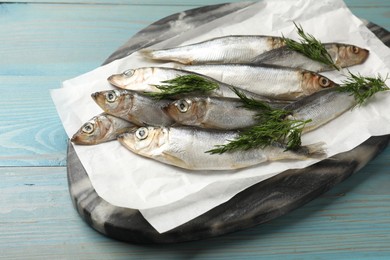 Photo of Fresh raw sprats and dill on light blue wooden table, closeup