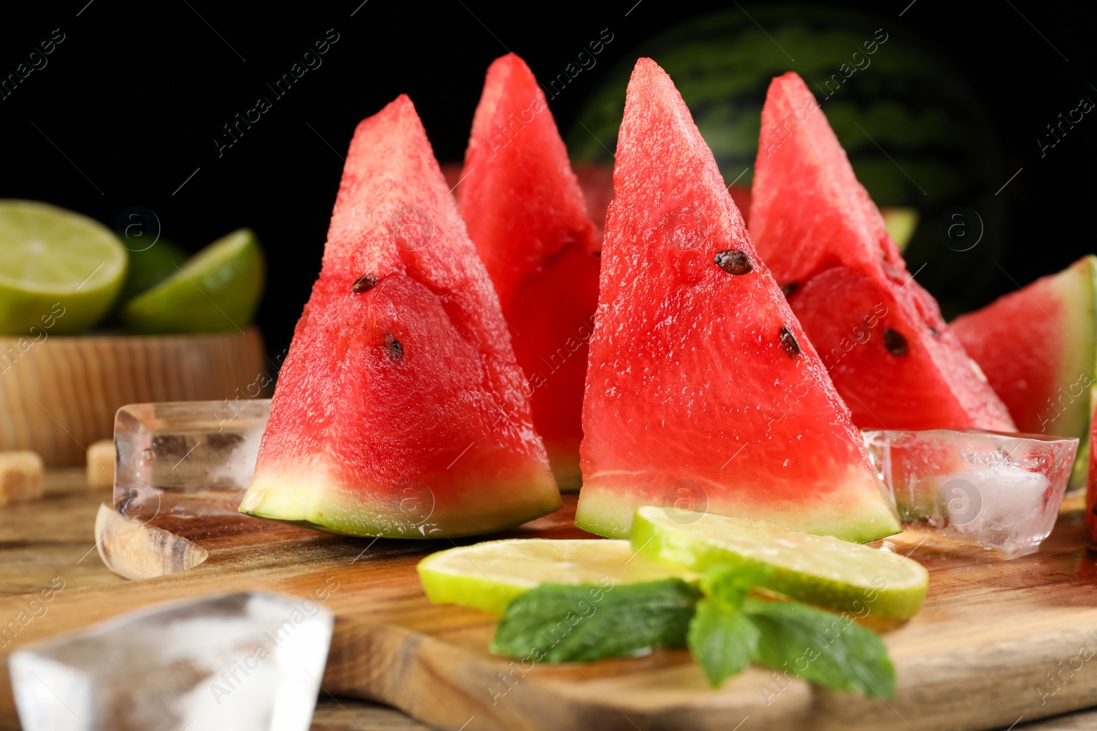 Photo of Board with juicy watermelon, ice and lime slices on wooden table, closeup