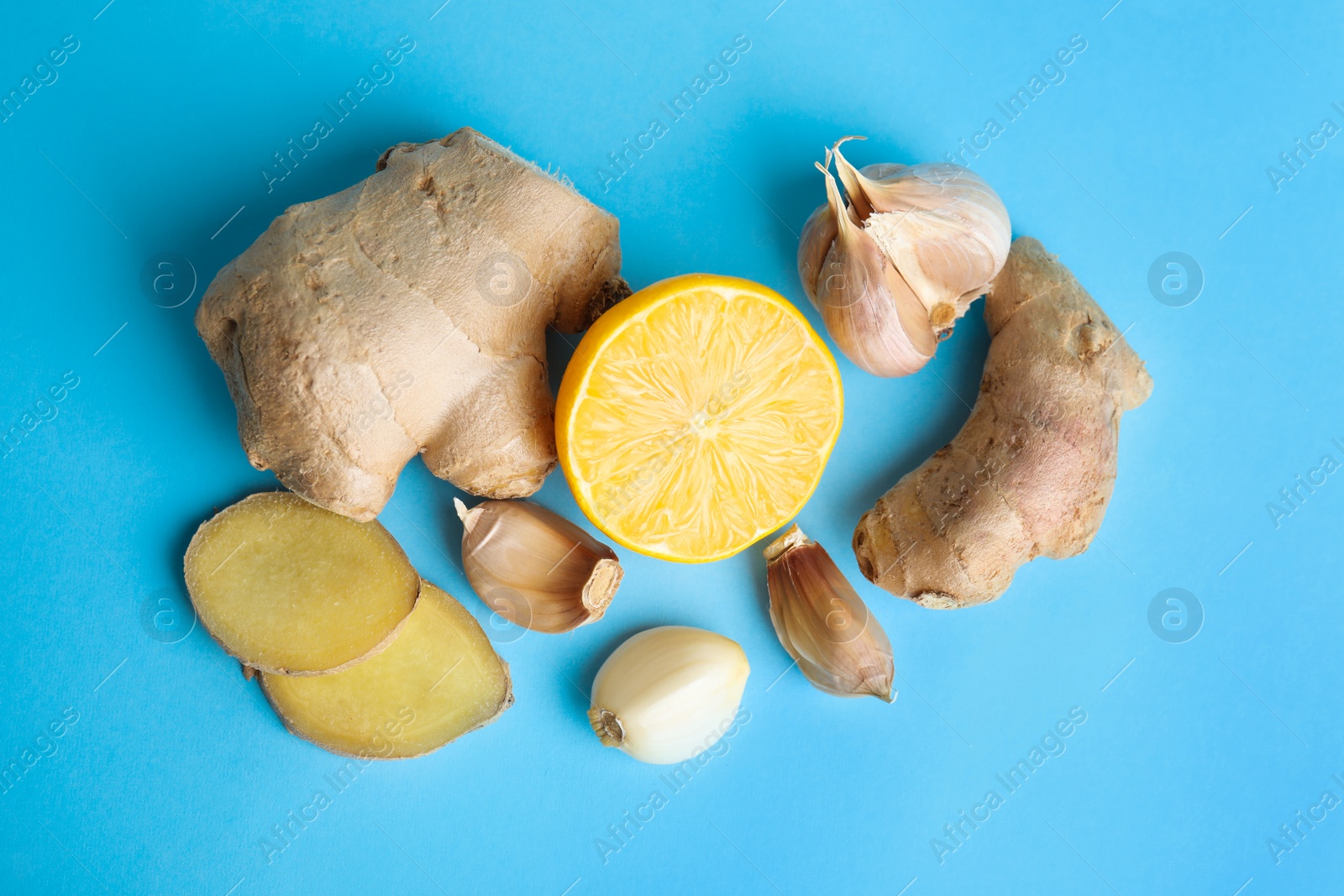 Photo of Fresh garlic and other natural cold remedies on light blue background, flat lay