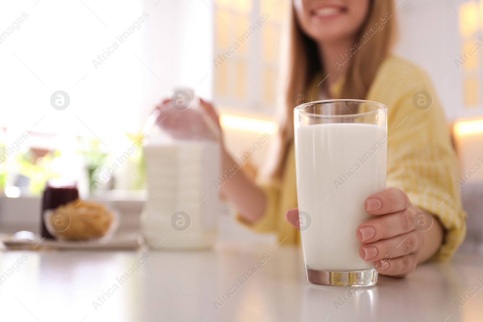 Photo of Young woman with gallon bottle of milk, glass and breakfast cereal at white table in kitchen, closeup