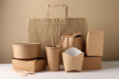 Photo of Eco friendly food packaging. Paper containers, tableware and bag on white table against beige background