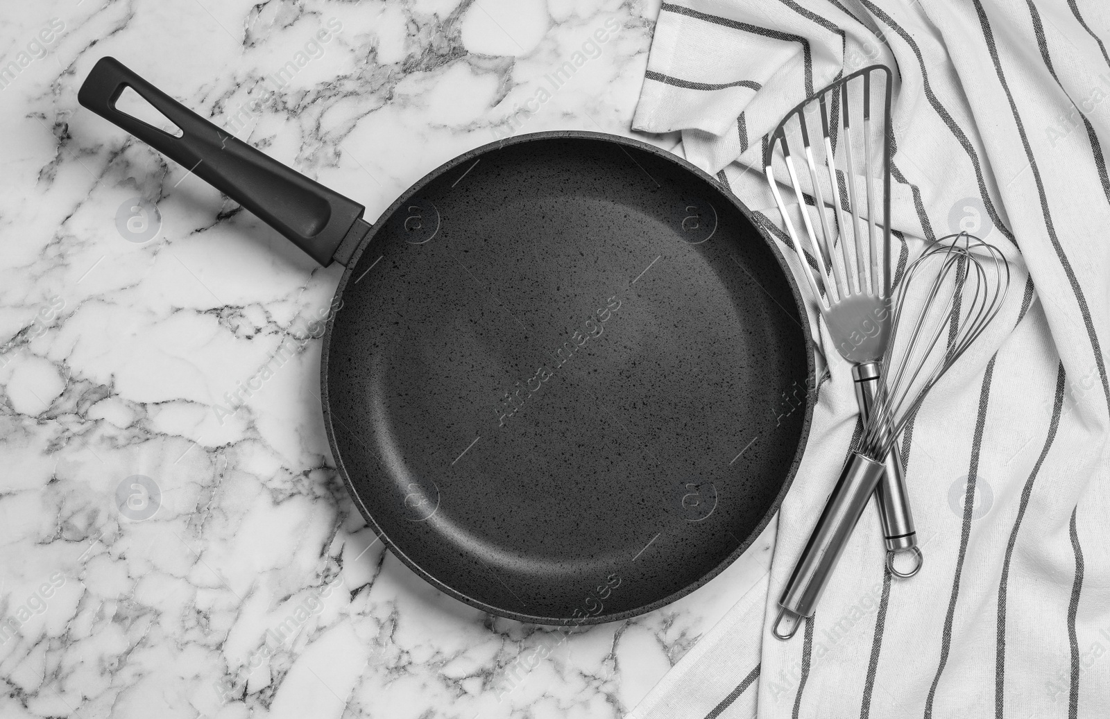 Photo of Frying pan, cooking utensils and tablecloth on white marble background, flat lay