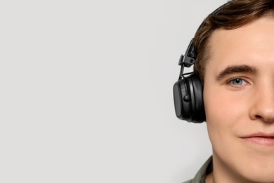 Photo of Handsome young man with headphones on light grey background, closeup. Space for text