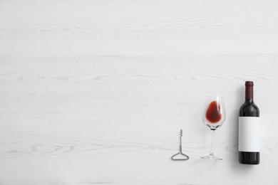 Flat lay composition with bottle of wine and elegant glass on white wooden background. Space for text