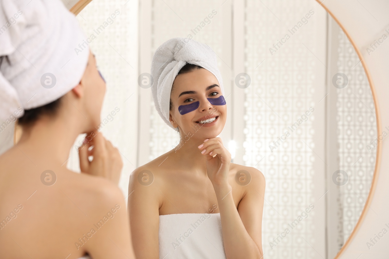 Photo of Beautiful young woman with under eye patches near mirror at home
