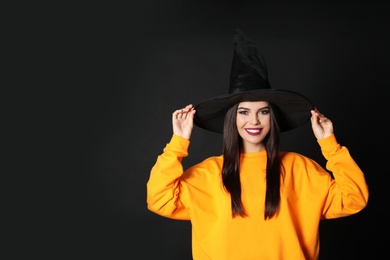 Photo of Beautiful woman wearing witch costume for Halloween party on black background, space for text