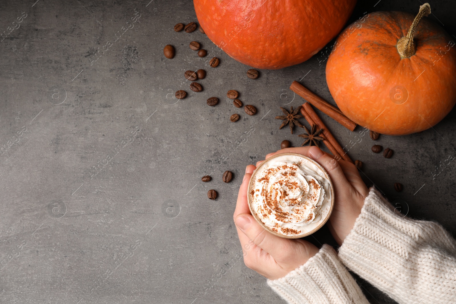 Photo of Woman holding cup of tasty pumpkin spice latte on gray table, flat lay with space for text