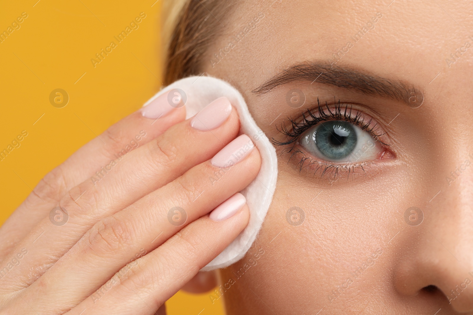 Photo of Beautiful woman removing makeup with cotton pad on orange background, closeup