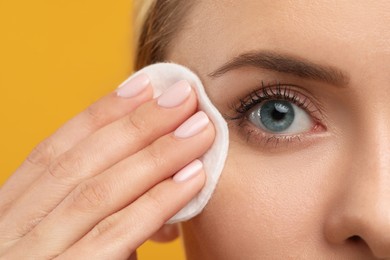 Photo of Beautiful woman removing makeup with cotton pad on orange background, closeup