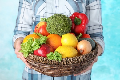 Photo of Woman holding wicker bowl with ripe fruits and vegetables on color background, closeup