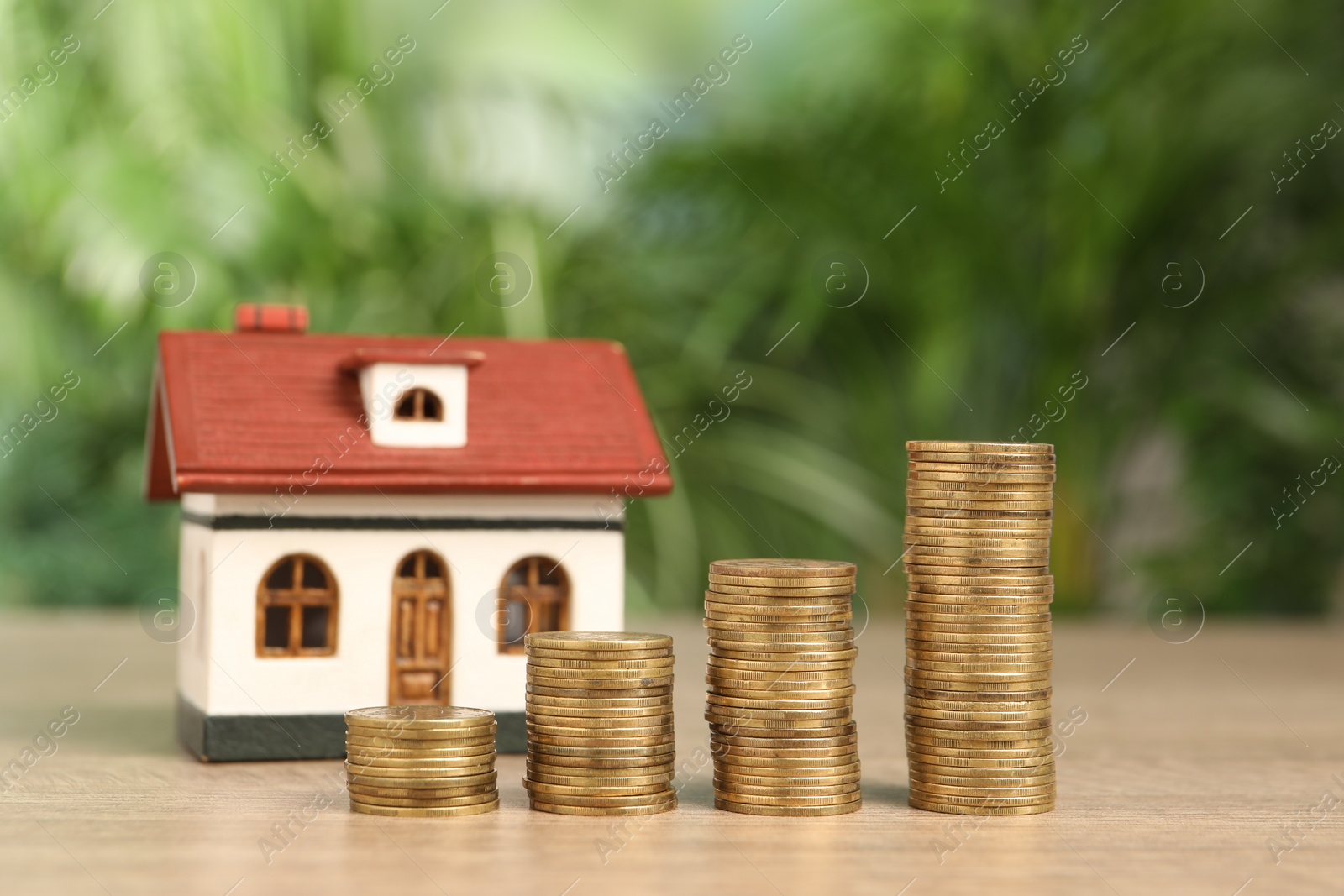 Photo of Mortgage concept. Model house and stacks of coins on wooden table against blurred green background