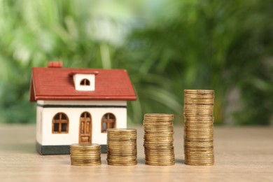 Photo of Mortgage concept. Model house and stackscoins on wooden table against blurred green background