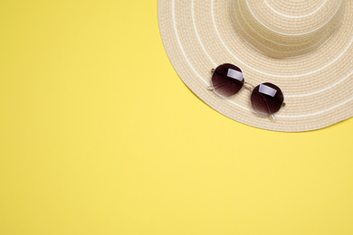 Hat and sunglasses on yellow background, top view with space for text. Beach objects